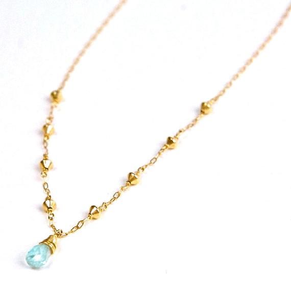 An ice blue topaz briolette is hand wrapped in 14k gold filled suspended by a hand beaded 14k gold filled chain.The simplicity of this pendant makes it a perfect everyday necklace.This necklace is made of high quality materials. We only use 14k gold filled and rose gold filled, which (unlike gold plate) will not wear off after multiple wears. All of our silver is argentium sterling silver, which is a higher quality version of sterling silver that is tarnish resistant and nickel free.Blue Topaz D Dainty Gold Topaz Jewelry, Gold Faceted Blue Topaz Necklaces, Gold Necklace With Faceted Blue Topaz, Gold Blue Topaz Birthstone Necklace, Blue Topaz Briolette Necklace For Gifts, Gold Necklace With Blue Topaz Briolette, Gold Briolette Blue Topaz Necklace, Gold Blue Topaz Teardrop Pendant, Gold Blue Topaz Drop Jewelry