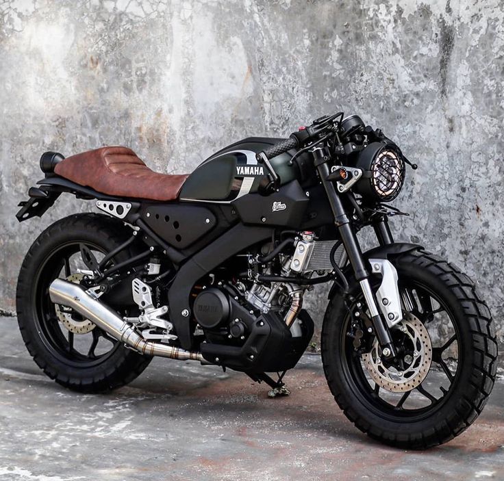 a black motorcycle parked in front of a concrete wall with a leather seat on it