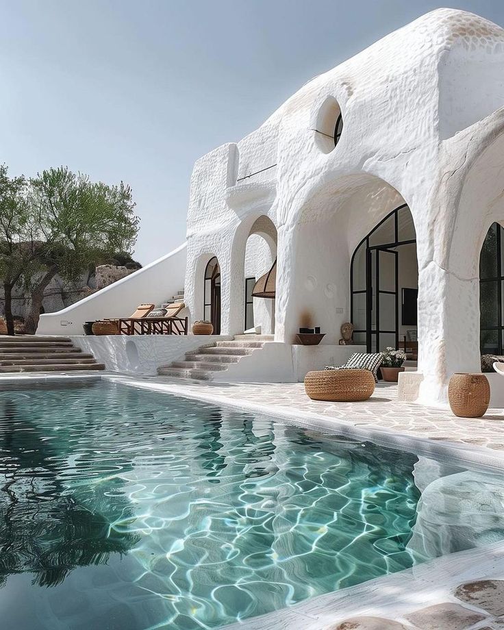 an outdoor swimming pool in front of a white building with steps leading up to it