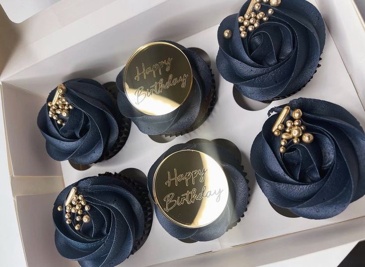 four cupcakes in a box with blue frosting and gold decorations on them