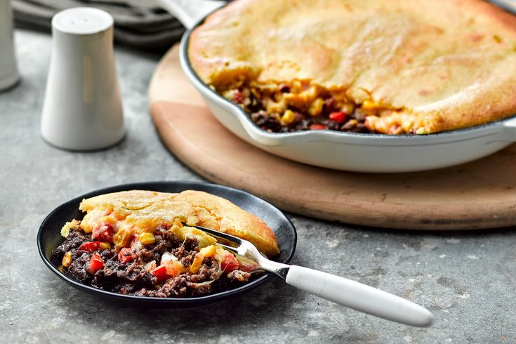 a pie with meat and vegetables is on a plate next to a bowl of soup