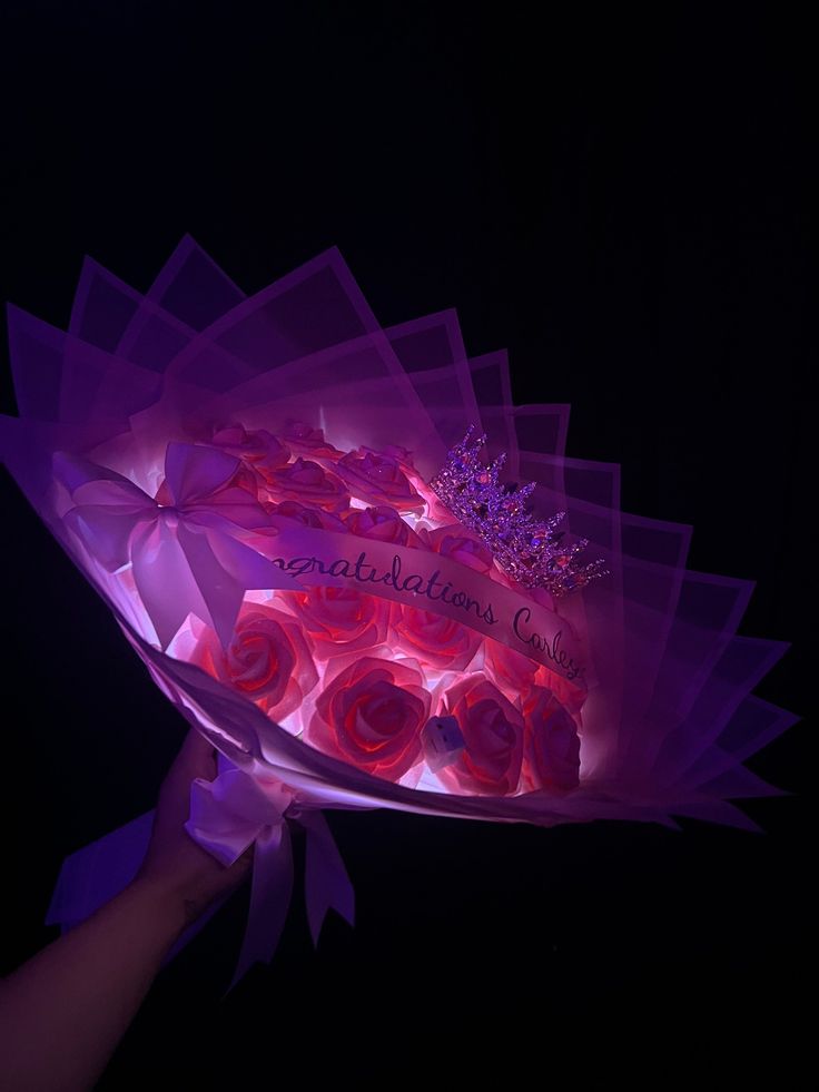 a person holding up a pink cake with roses on it in front of a black background