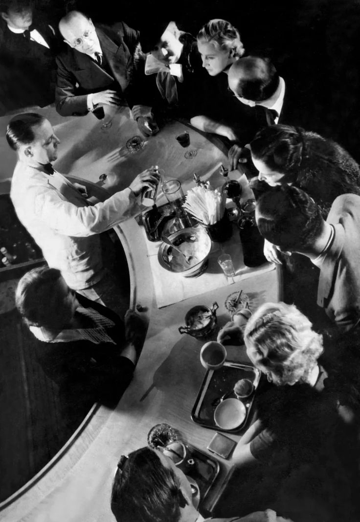 a group of people sitting around a table with plates and cups on it, all looking at something in the distance