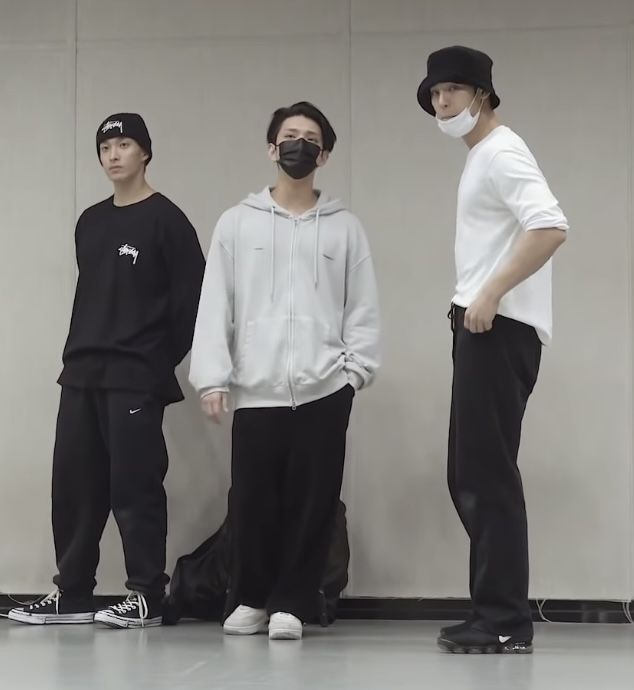 three young men standing next to each other in front of a wall wearing face masks