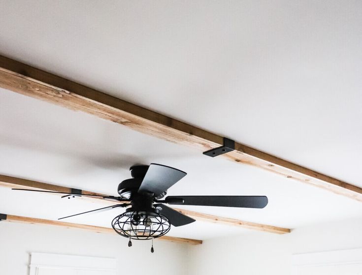 a ceiling fan is hanging from the ceiling in a room with white walls and wood beams