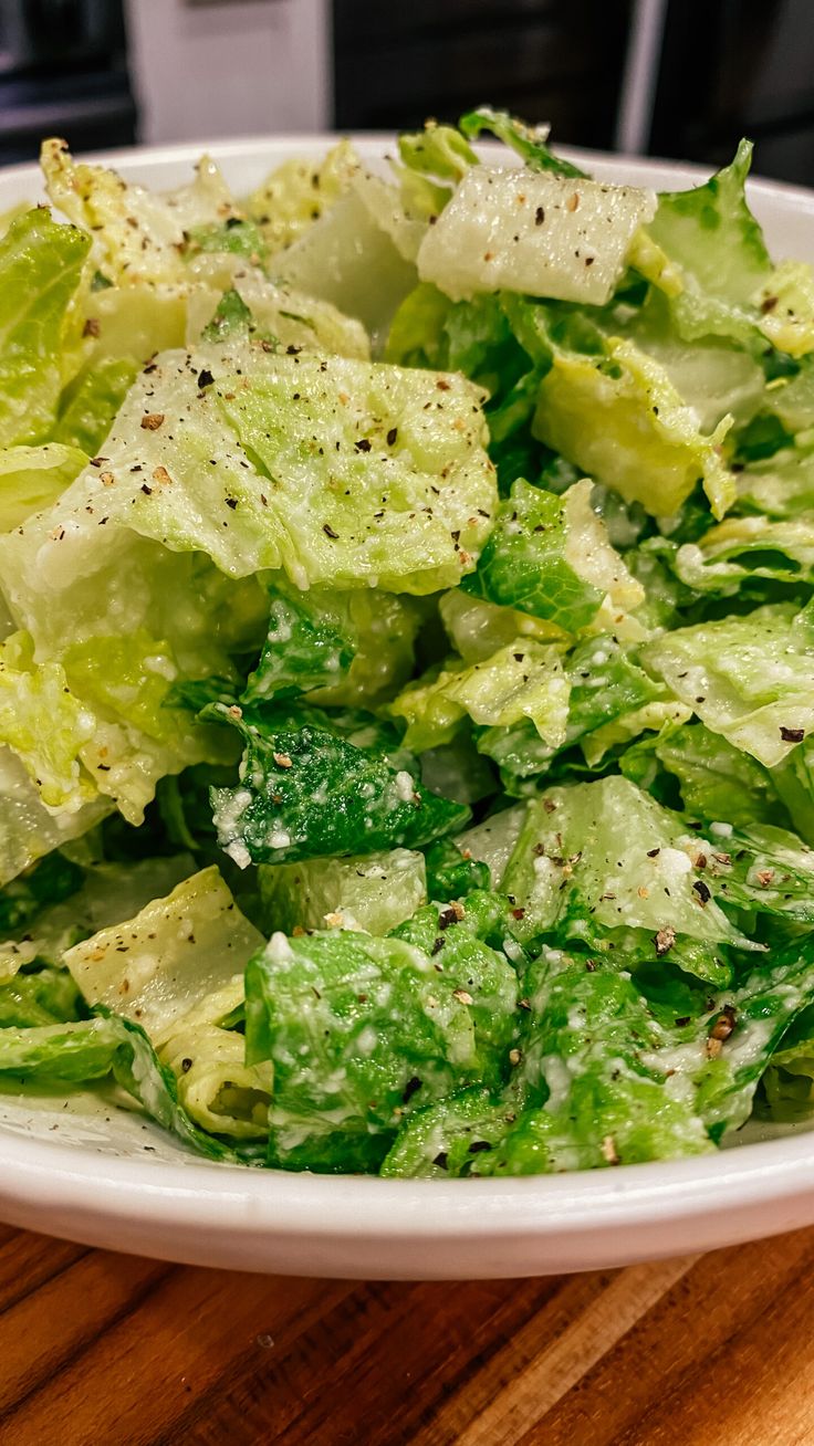 a white bowl filled with lettuce on top of a wooden table