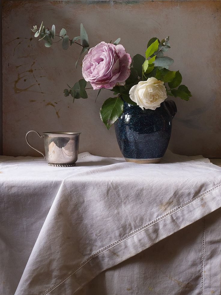 a blue vase with pink and white flowers on a table next to a silver cup