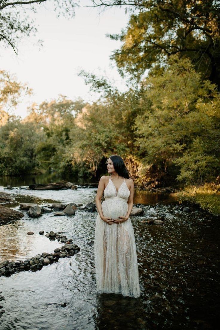 a pregnant woman standing in the middle of a river with her hands on her belly