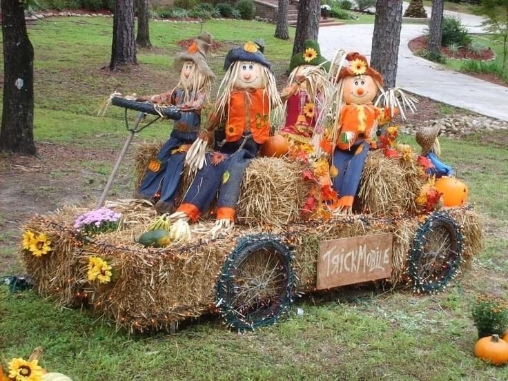 three scarecrows are sitting on hay in a wagon with pumpkins and sunflowers