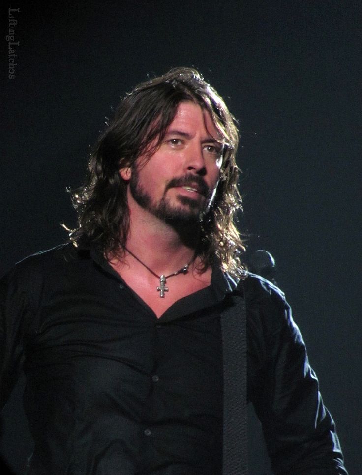 a man with long hair wearing a black shirt and holding a guitar in his hand