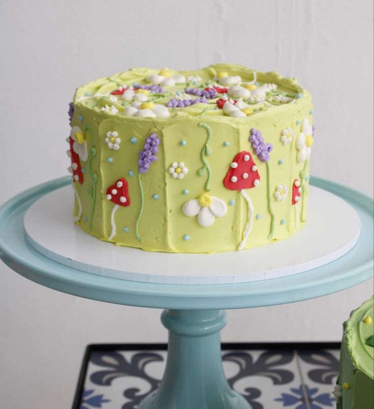 a green cake with mushrooms and flowers on it is sitting on a blue stand next to a white wall