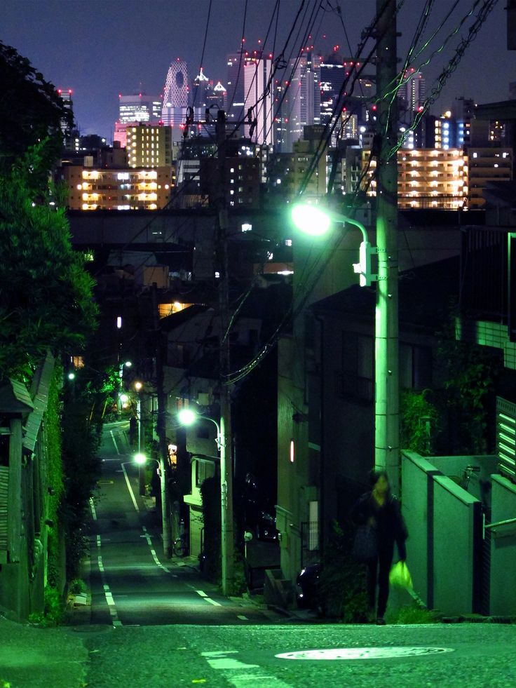 a person walking down an alley way at night with the city lights in the background