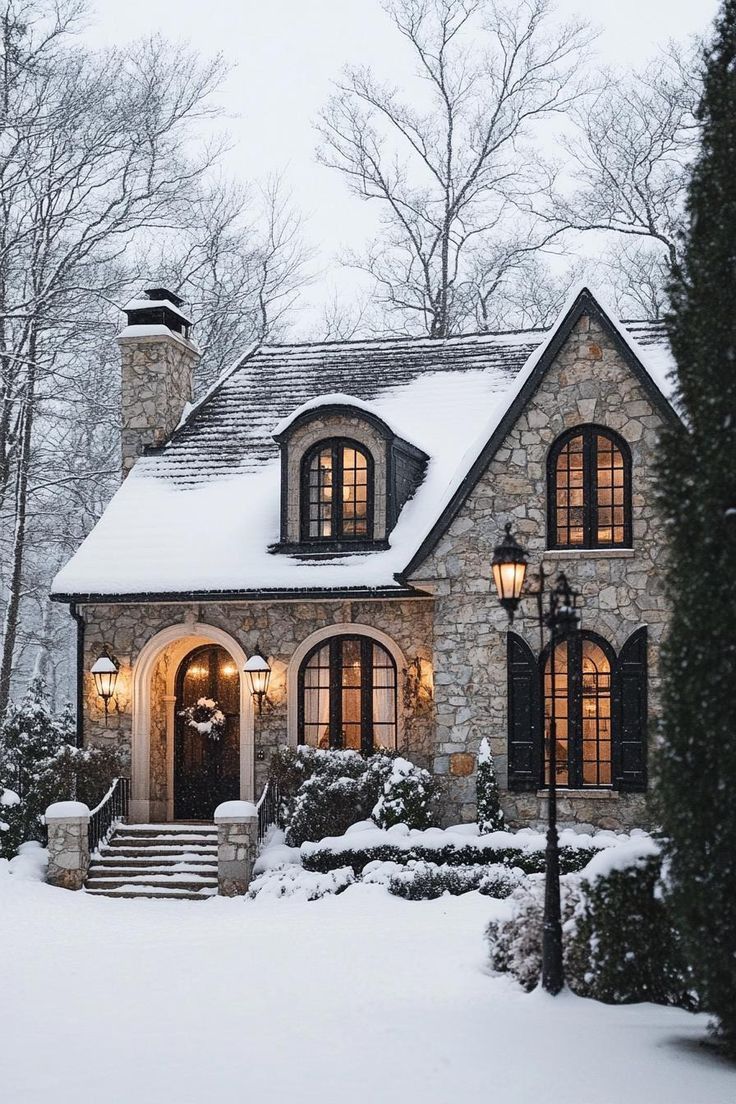 a stone house is covered in snow and lit up by two large lights on the front door