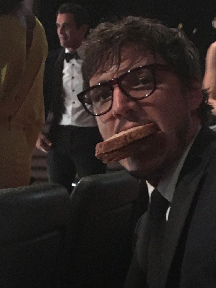 a man wearing glasses and eating food in front of other people at an awards event