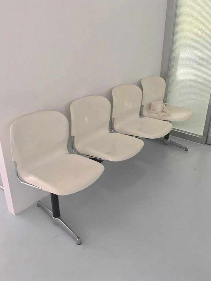 four white chairs are lined up against the wall in an office space with glass doors