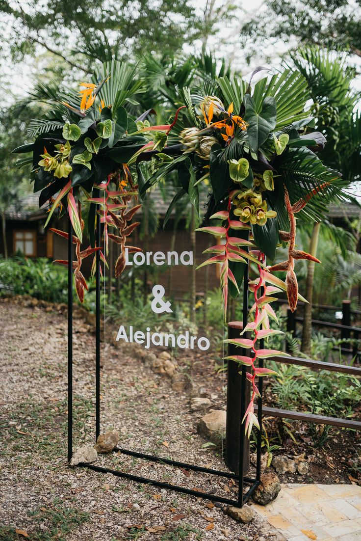 an arch decorated with flowers and greenery stands in front of a sign that reads lorena & alegandro