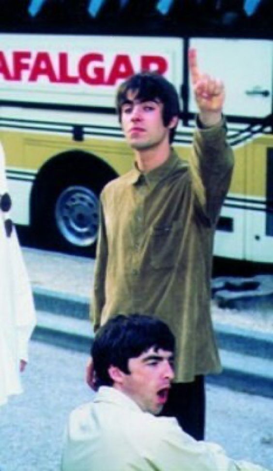 two men sitting on the ground in front of a bus and one man pointing at something