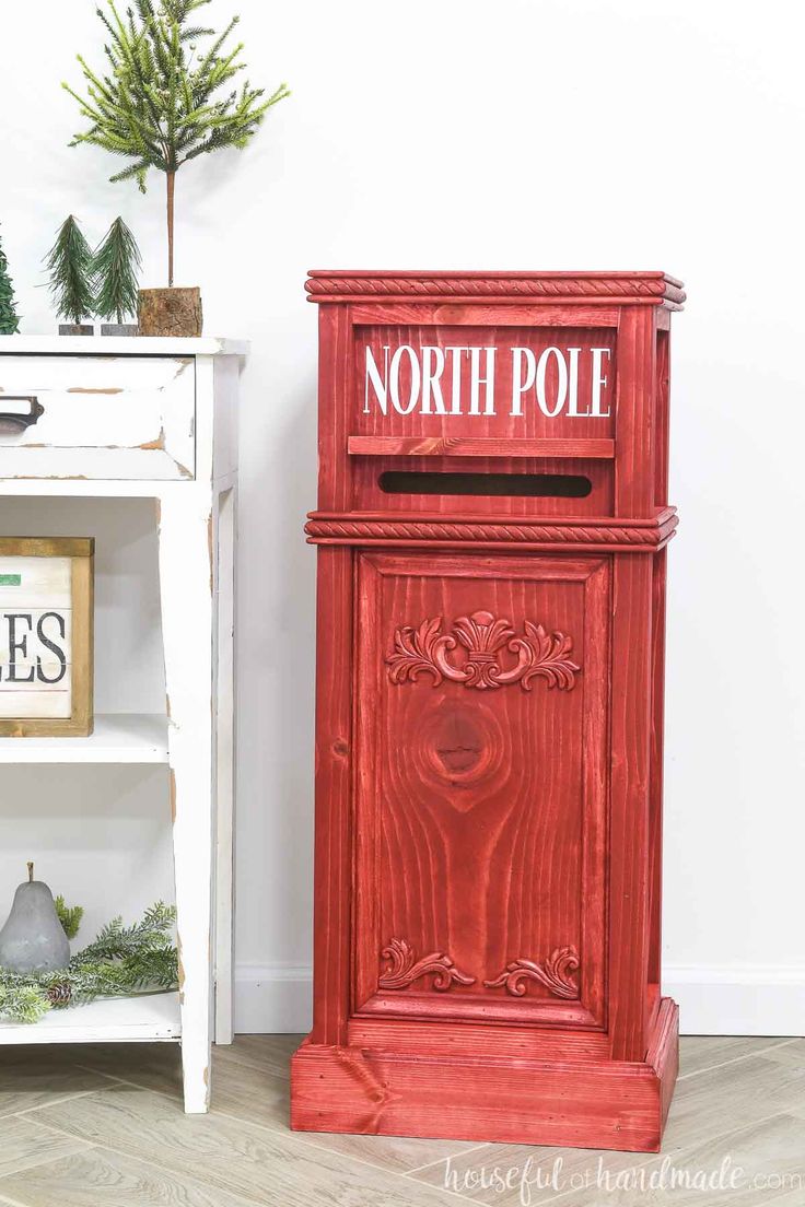 a red wooden mailbox sitting next to a white shelf with christmas decorations on it