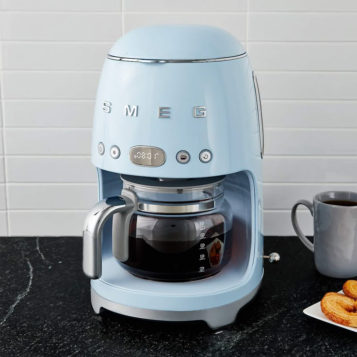 a blue coffee maker sitting on top of a counter next to a plate of food