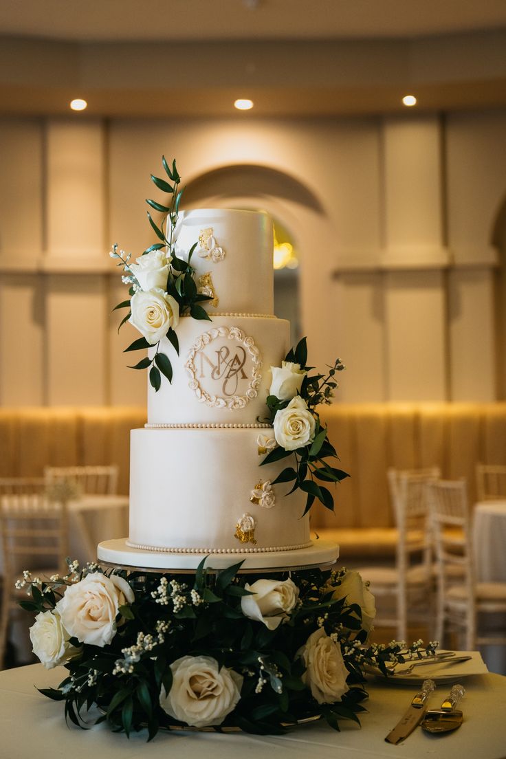 a wedding cake with white flowers and greenery on the table in front of it