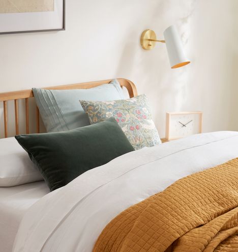 a bed with pillows and blankets on it next to a wall lamp in a bedroom