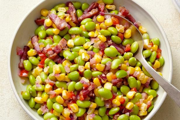 a white bowl filled with green beans and bacon on top of a table next to a spoon