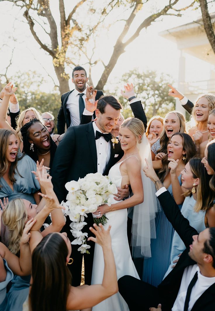 a bride and groom are surrounded by their wedding party in front of the cameraman