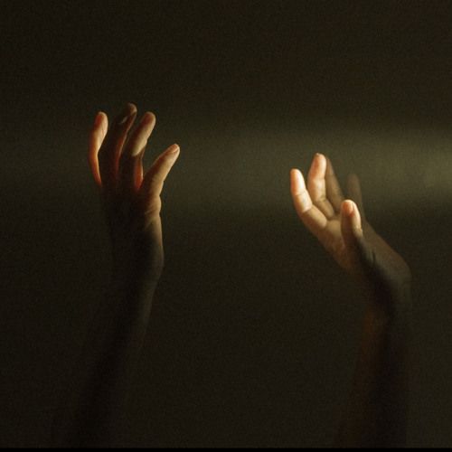 two hands reaching up in the air to catch something with their fingers, against a dark background