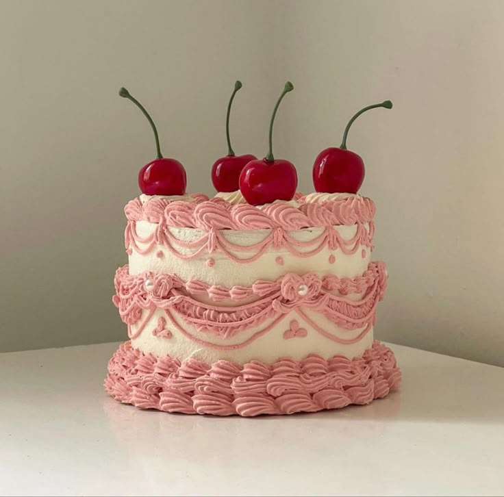 a cake with pink icing and cherries on top is sitting on a table