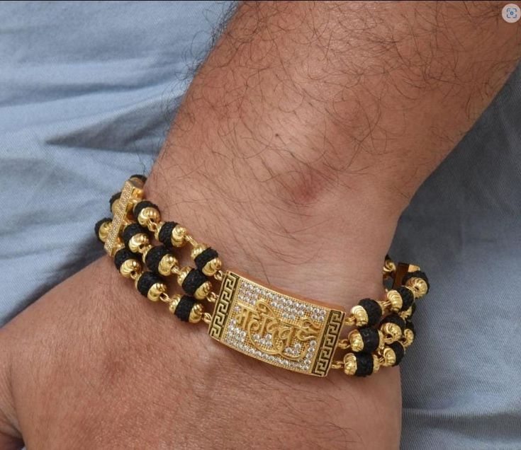 The Mahadev Design Gold Plated Rudraksha Bracelet is a timeless accessory for men. Crafted from brass and plated with gold, this textured design features diamond etching, a shining Rudraksha bead, and a black-hued bracelet for a spiritual yet stylish look. 100% Hid_Reg_Plating ensures lasting shine and durability. Bracelet Dimension Height:20 cm (7.87 inch) Width:17 mm (1.7 cm) Depth:3 mm (0.3 cm) Other Specification Weight:20 Gram Size:Fixed Lock Type:Fold Over / Flap Over Color:Golden, Black M Mens Gold Bracelets Latest Rudraksh, Man Gold Bracelet Design, Rudraksha Bracelet, Mangal Sutra, Rudraksha Beads, Mens Gold Jewelry, Mens Gold Bracelets, Textured Design, Mens Gold