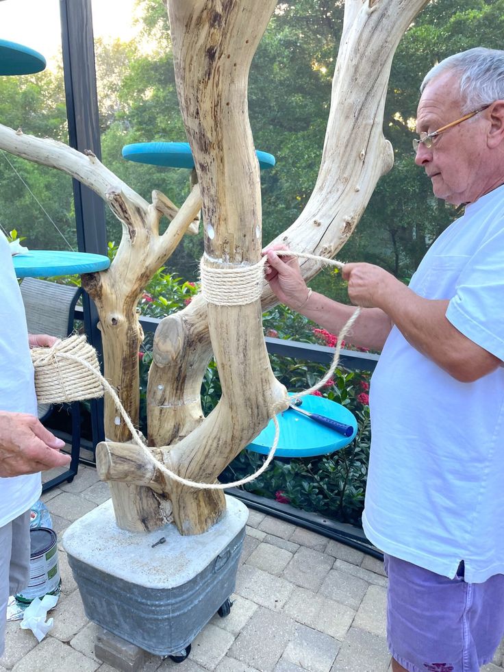 two men are working on a tree that has been made out of driftwood and rope