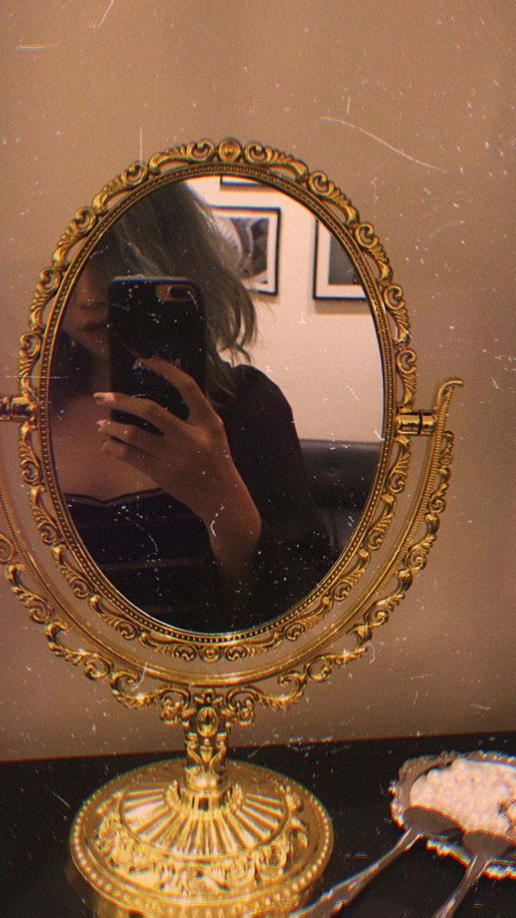 a woman taking a selfie in front of a mirror with gold trimmings