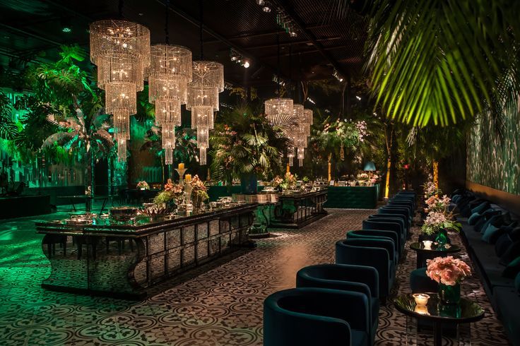 a room filled with lots of tables covered in lights and greenery next to tall palm trees