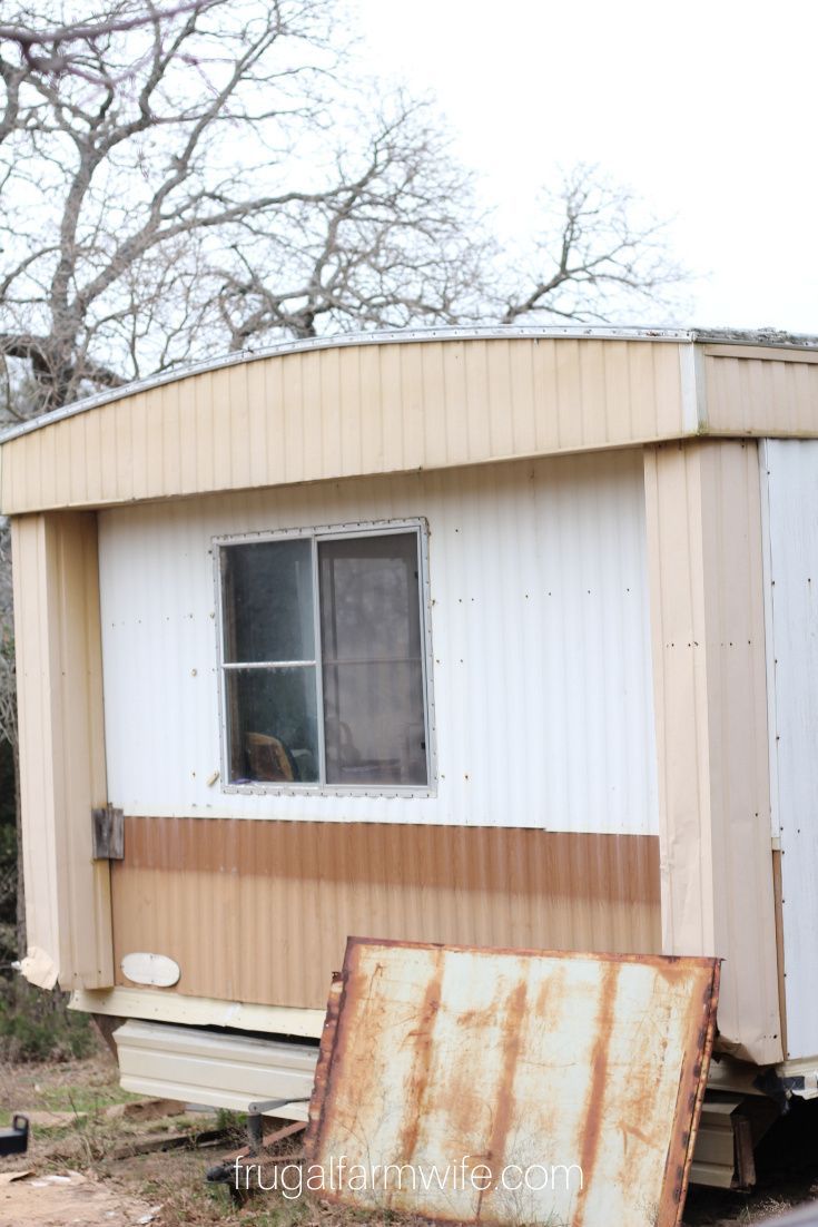 an old rusted out trailer sitting in front of a house with a broken window