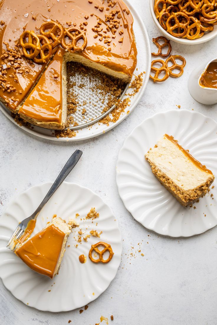 two plates with slices of cheesecake and caramel sauce on them next to pretzels