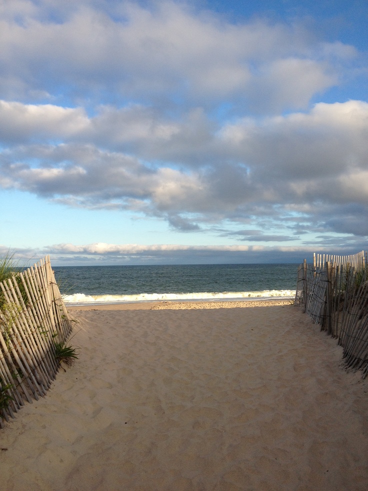 a sandy path leading to the ocean on a cloudy day