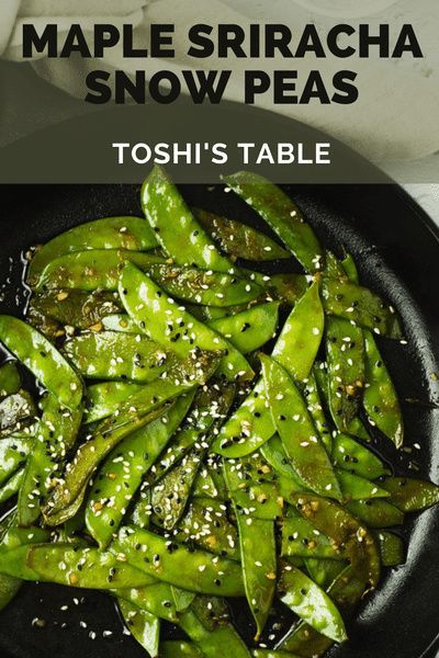 a black plate topped with green beans covered in sesame seeds