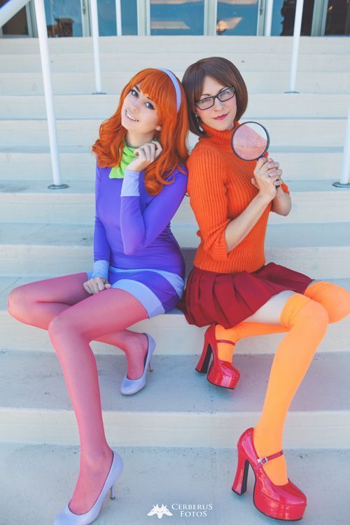 two women dressed in colorful outfits sitting on steps holding magnifying glasses and looking at the camera