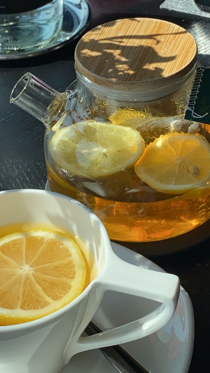 a cup of tea with lemon slices in it and a pitcher of water on the side