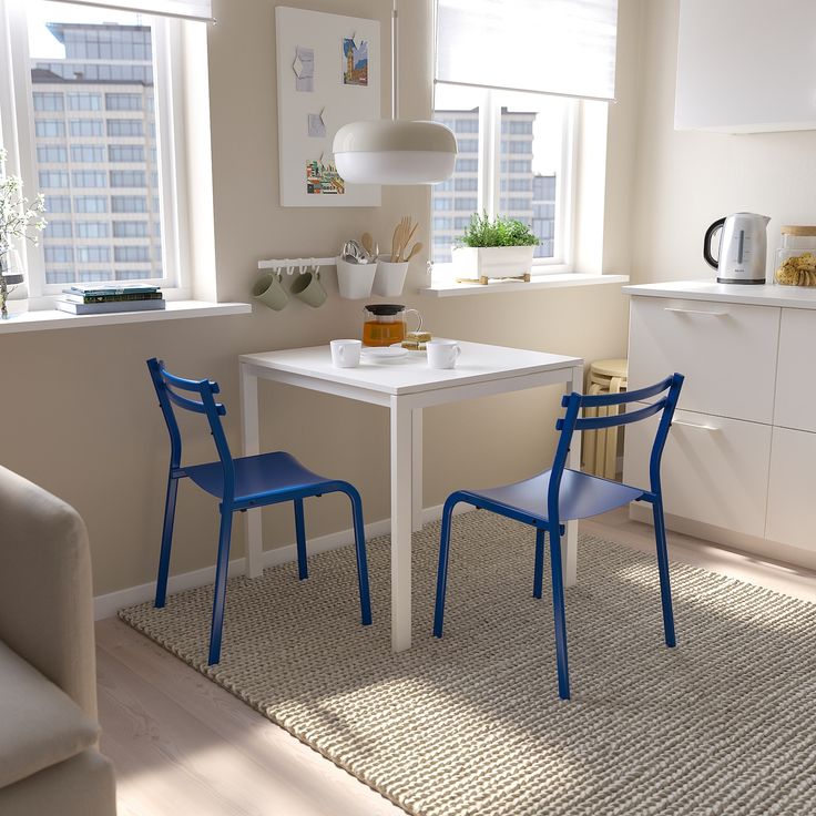 two blue chairs sitting at a white table in a living room next to a window