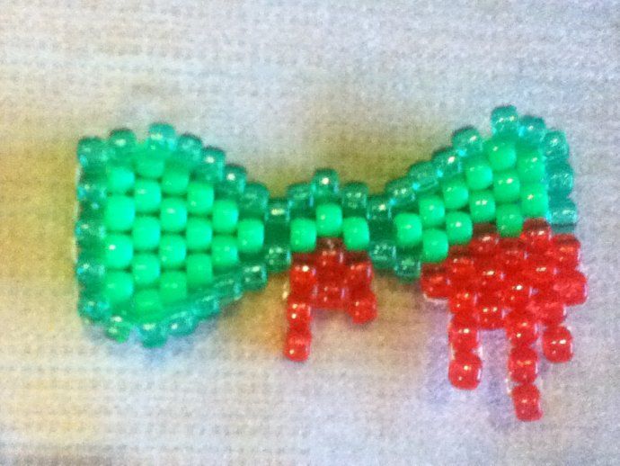 two bows made out of beads sitting on top of a white sheet with red, green and blue beads