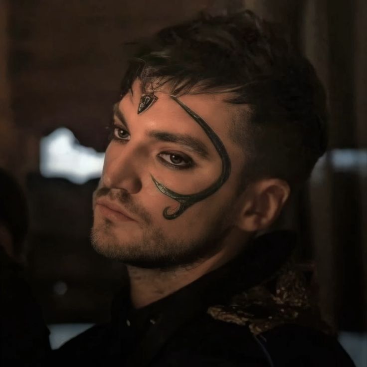 a man with his face painted in black and silver, looks into the distance while standing next to another man