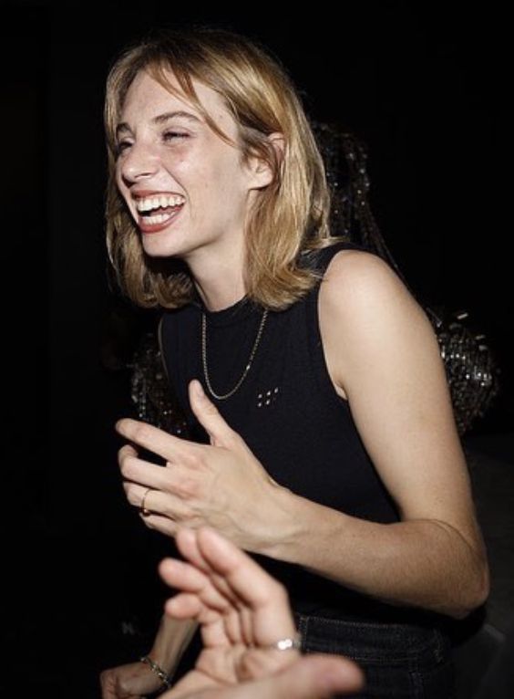 two women laugh as they talk to each other in a dark room with people around them