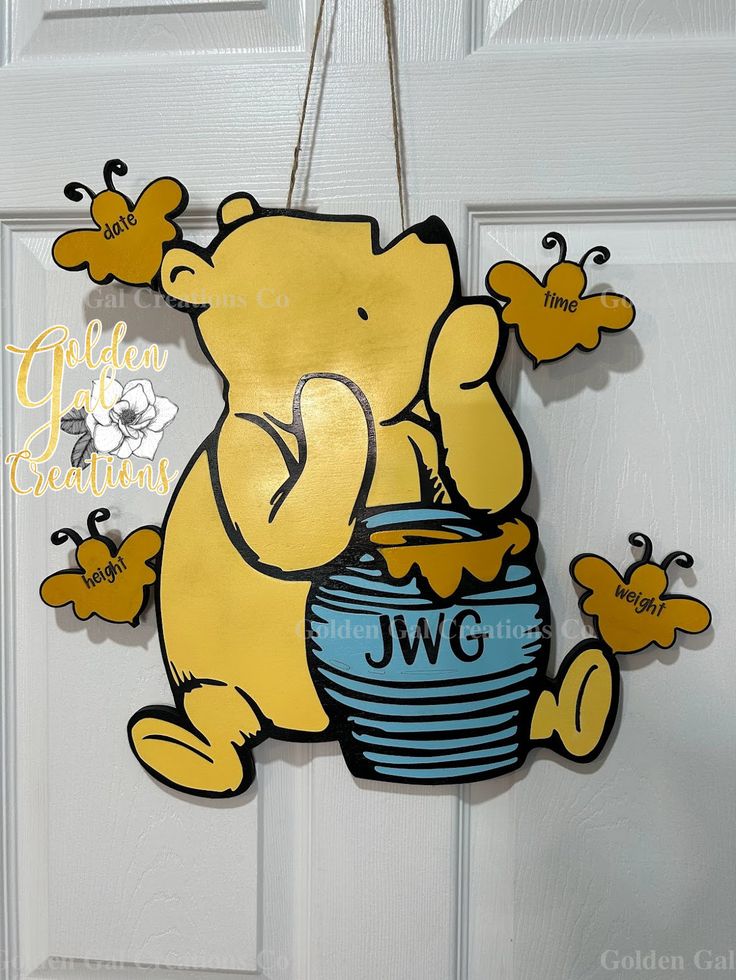 a yellow bear hanging from a door holding a blue bowl with honey bees on it