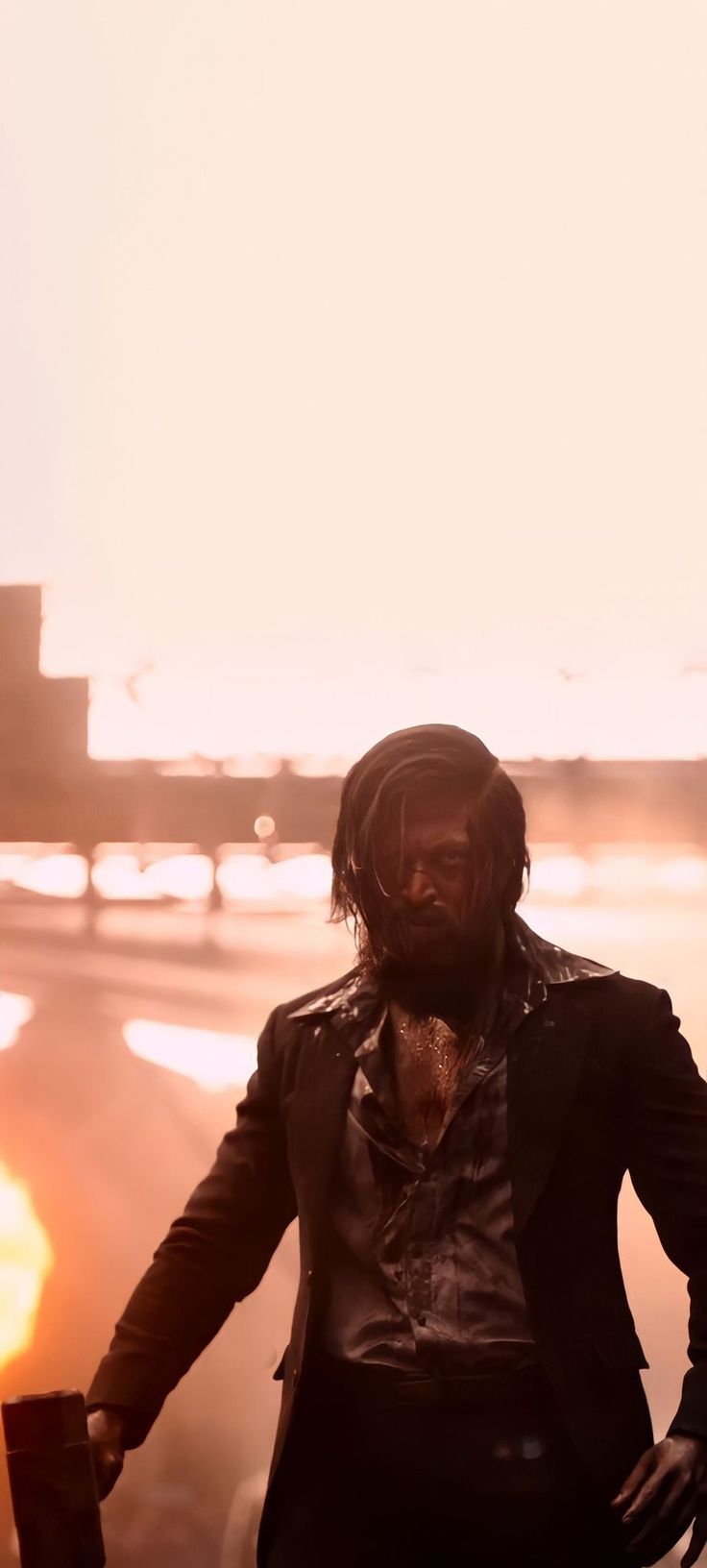 a man with dreadlocks standing next to the ocean in front of an orange sunset