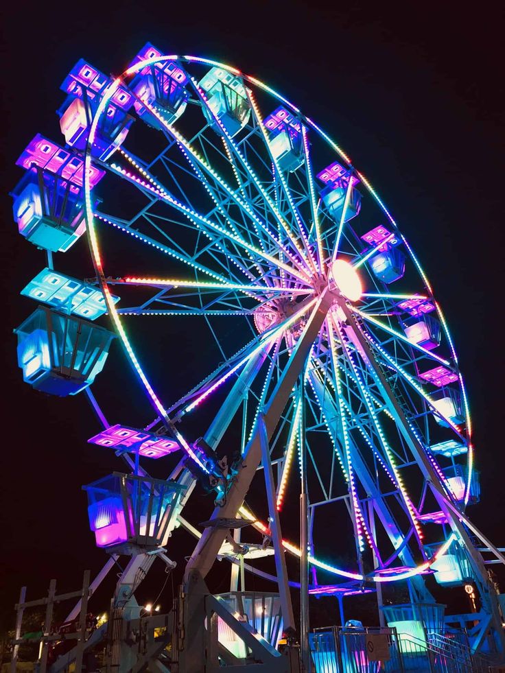 a ferris wheel lit up at night with bright lights on it's sides and the sky in the background