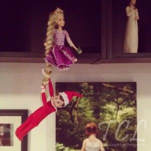 two barbie dolls hanging from the ceiling in a room with pictures on the wall behind them