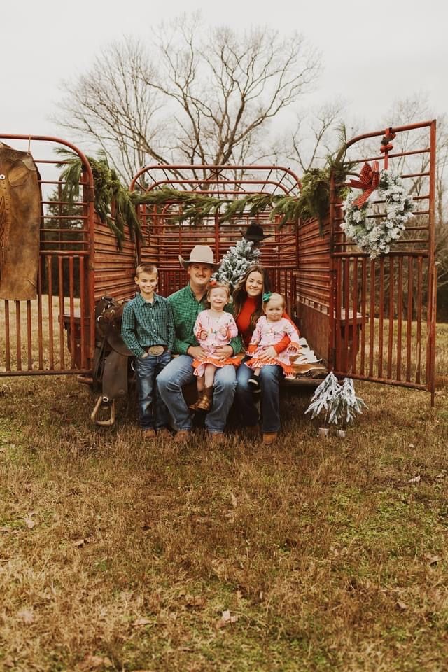 a family sitting on a bench in front of a gate with christmas wreaths and decorations