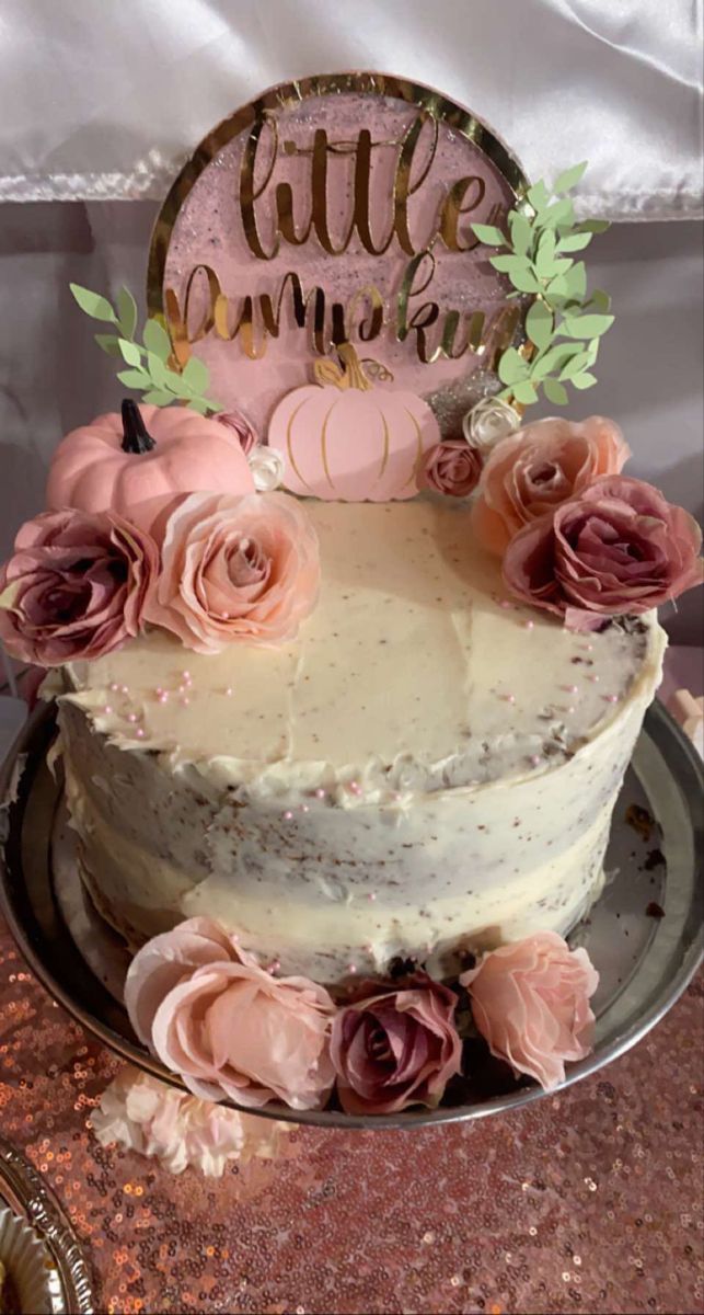 a white cake with pink flowers and a little pumpkin sign on top that says little pumpkin