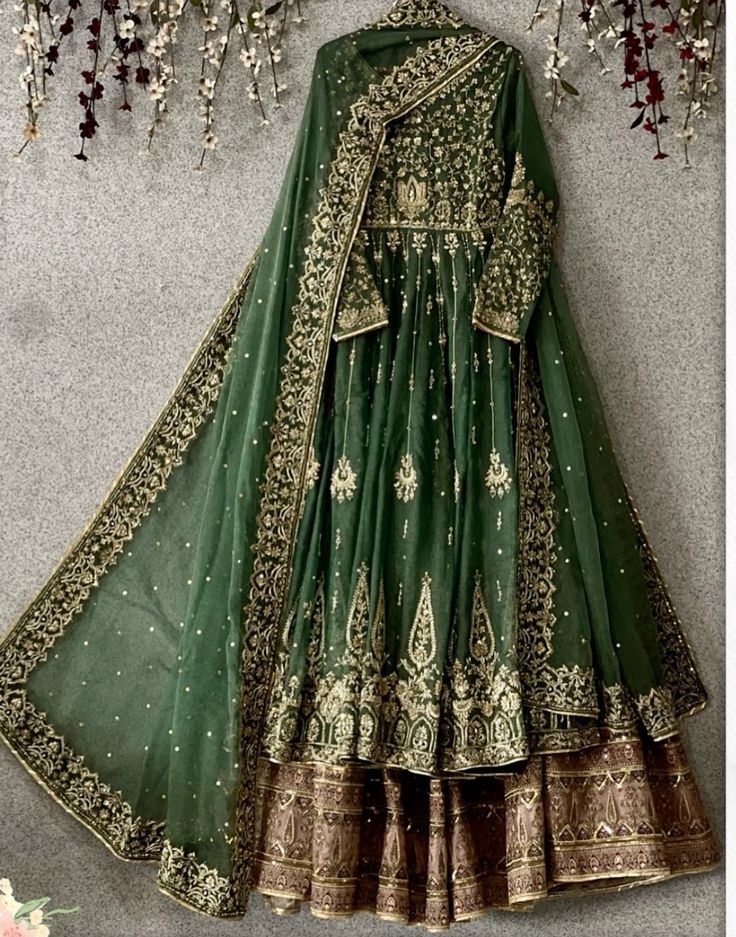 a green and gold lehenga is hanging on the wall next to some flowers